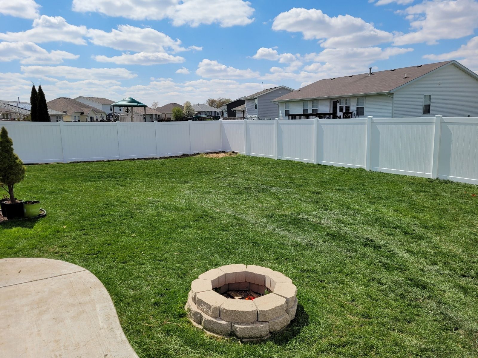 A backyard with a fire pit and a white fence.