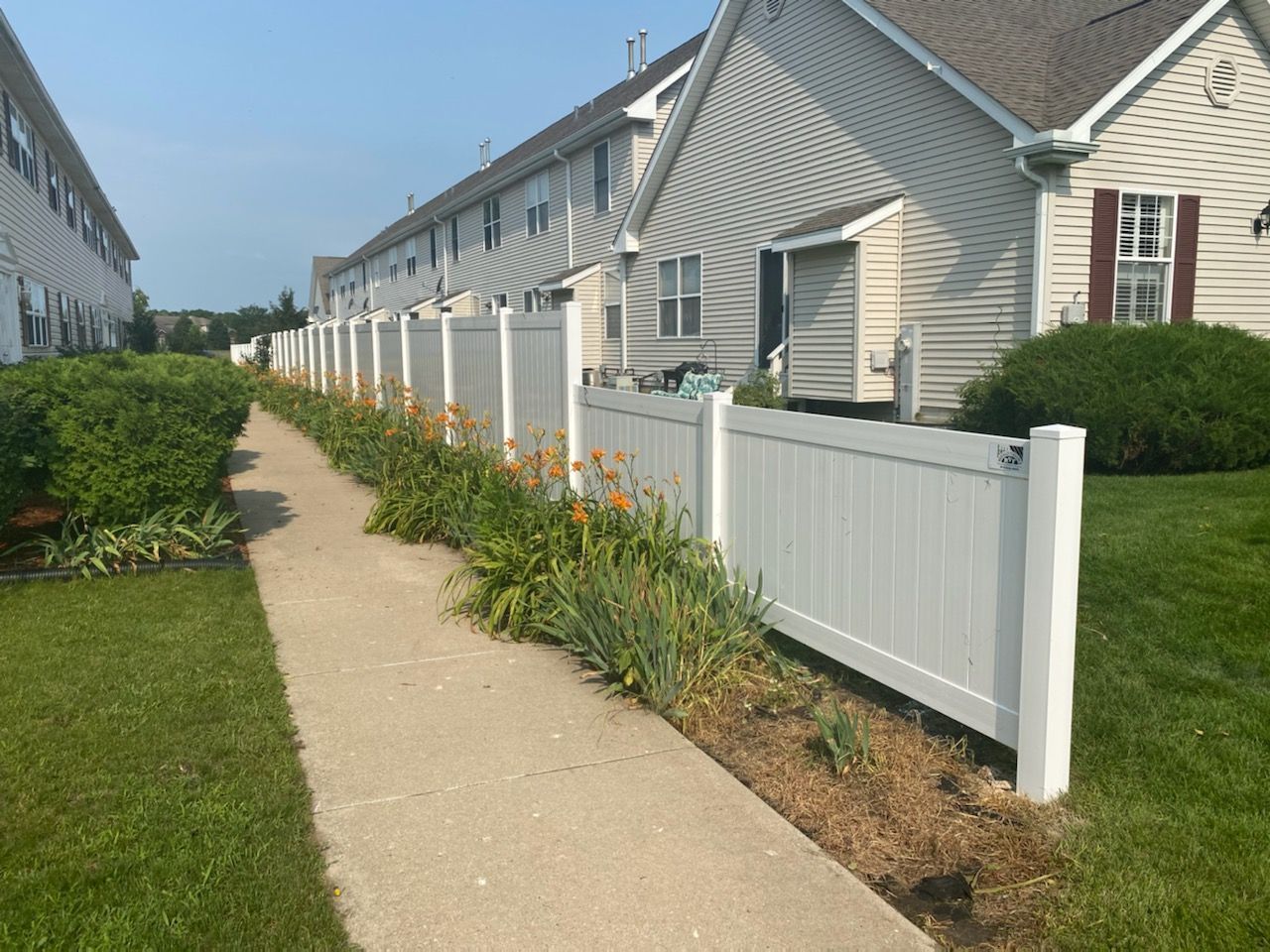 A white fence along a sidewalk in front of a row of houses.