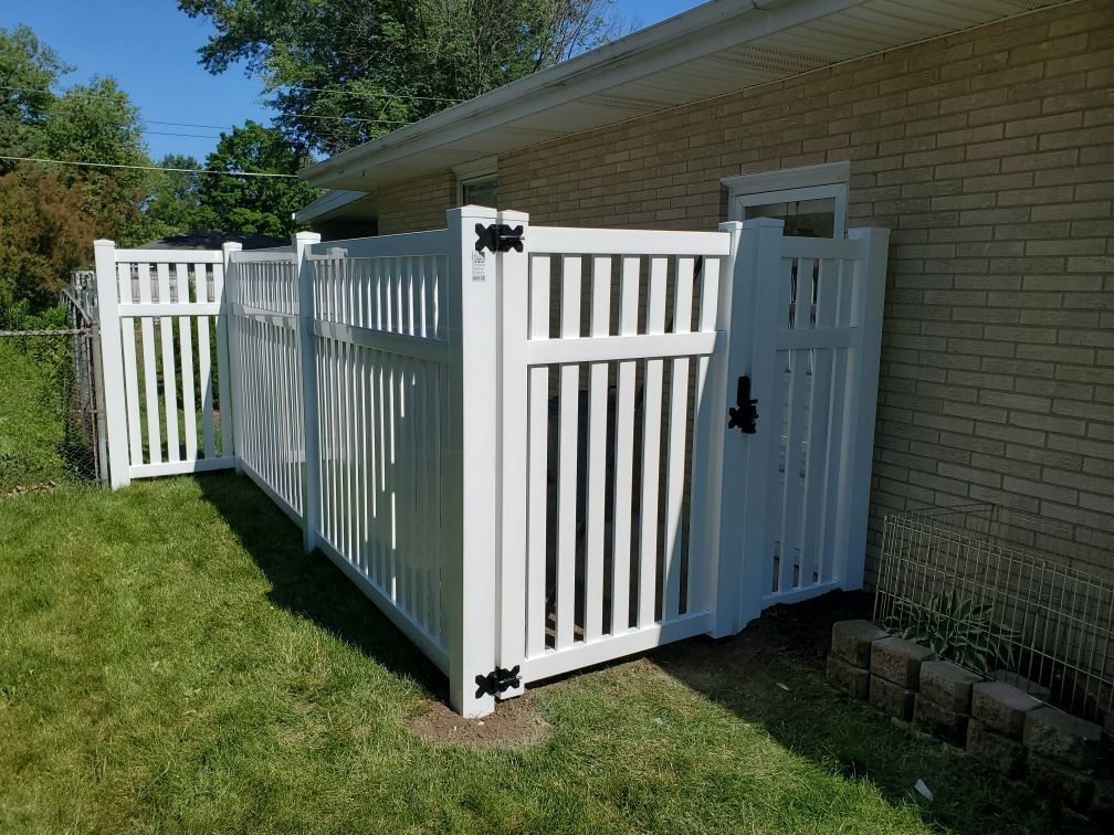 A white fence with a gate in front of a brick house.