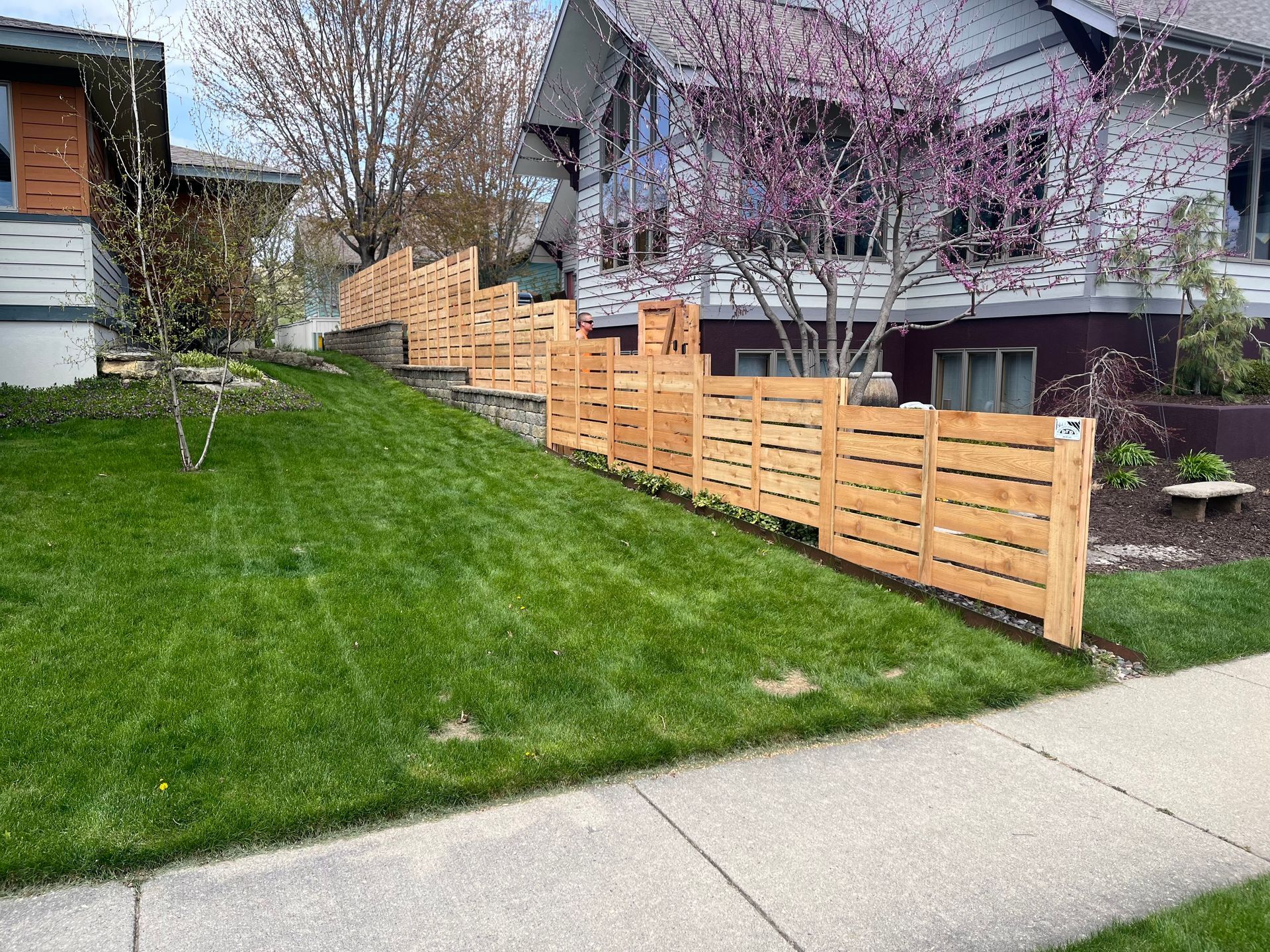A wooden fence surrounds a lush green lawn in front of a house.