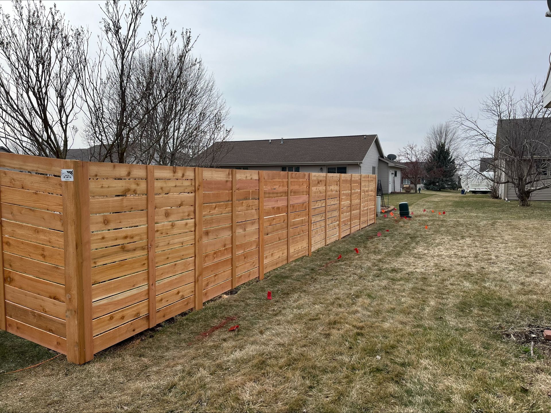 A wooden fence is sitting in the middle of a grassy field next to a house.