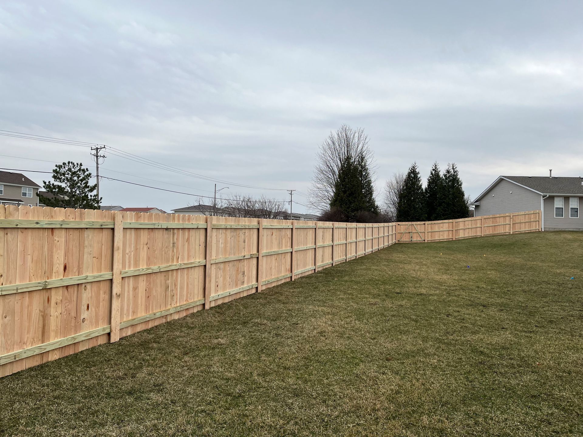 A wooden fence surrounds a lush green field in front of a house.