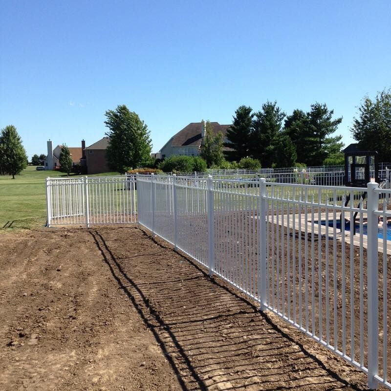 A white fence surrounds a swimming pool with a house in the background