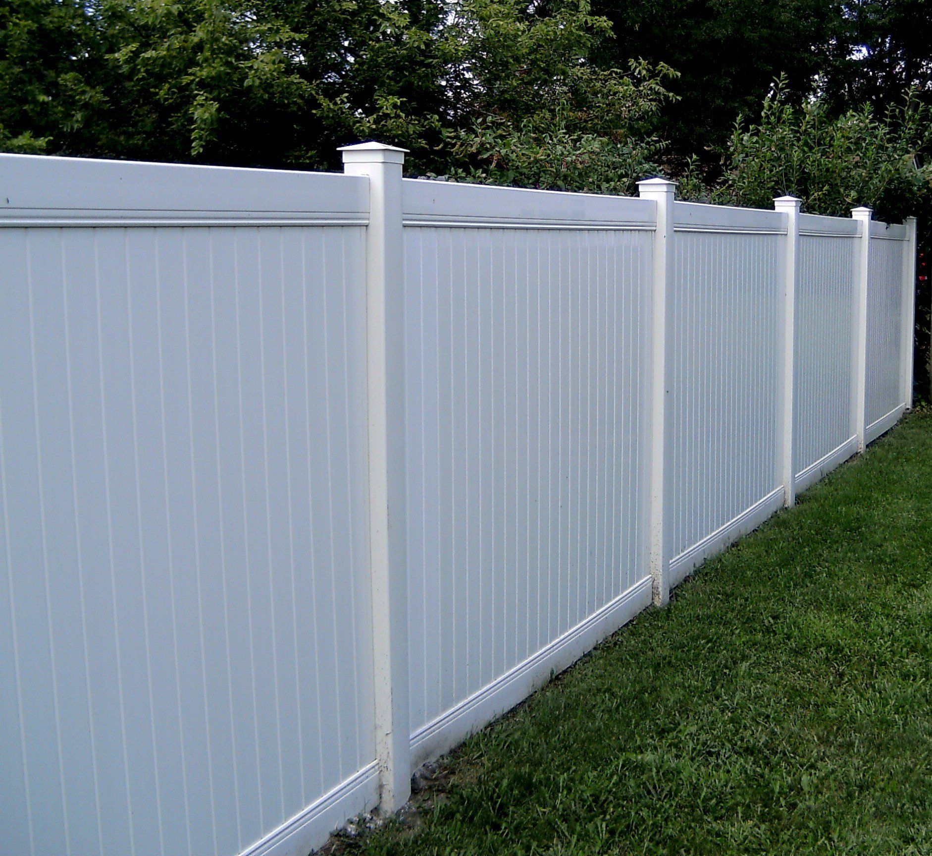 A white fence is surrounded by green grass and trees.