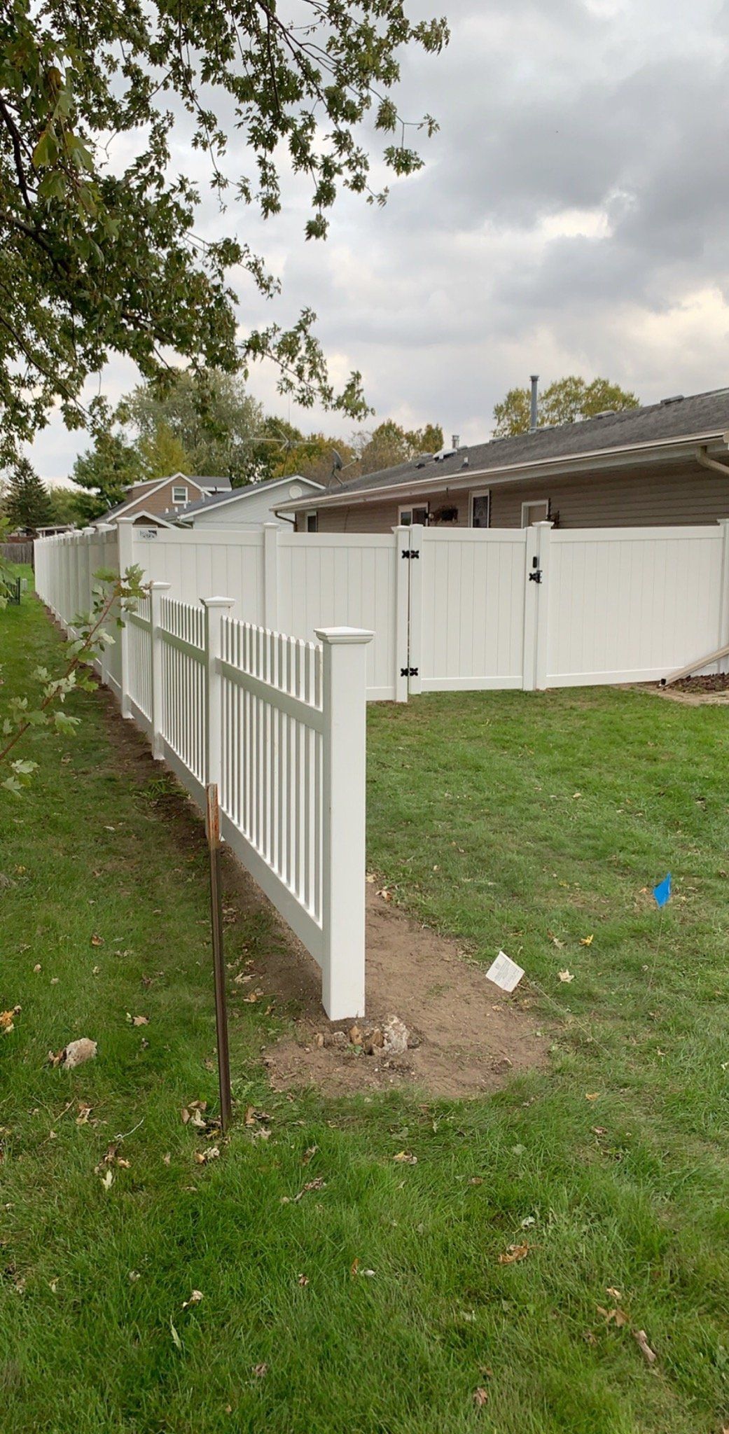 A white fence surrounds a lush green yard in front of a house.