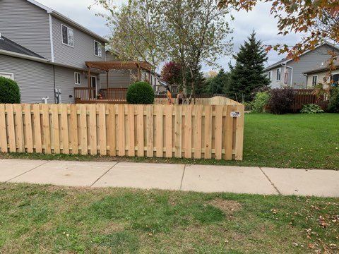 A wooden fence surrounds a lush green yard in front of a house.