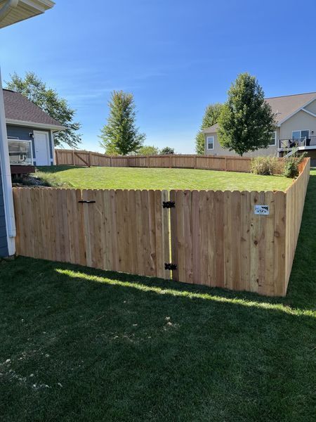 A wooden fence surrounds a lush green yard with a house in the background.
