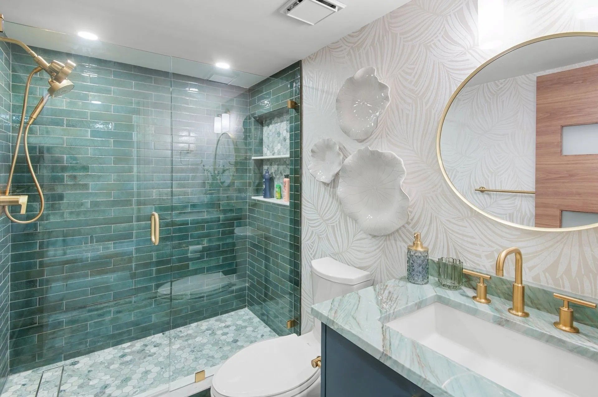Modern bathroom with a glass-enclosed shower featuring green subway tiles, a blue vanity, and a round wall mirror.
