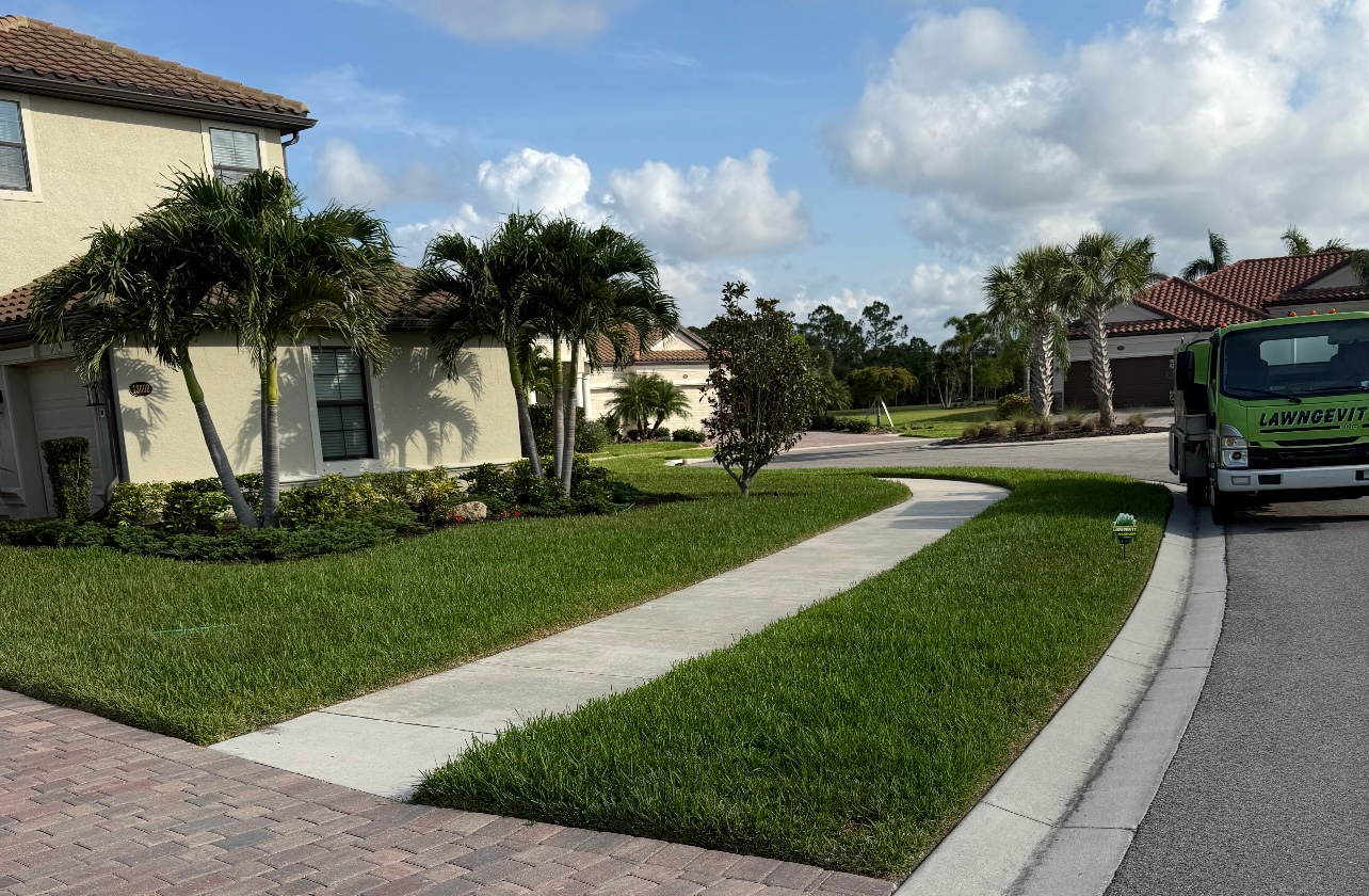 A green truck is parked on the side of the road in front of a house.