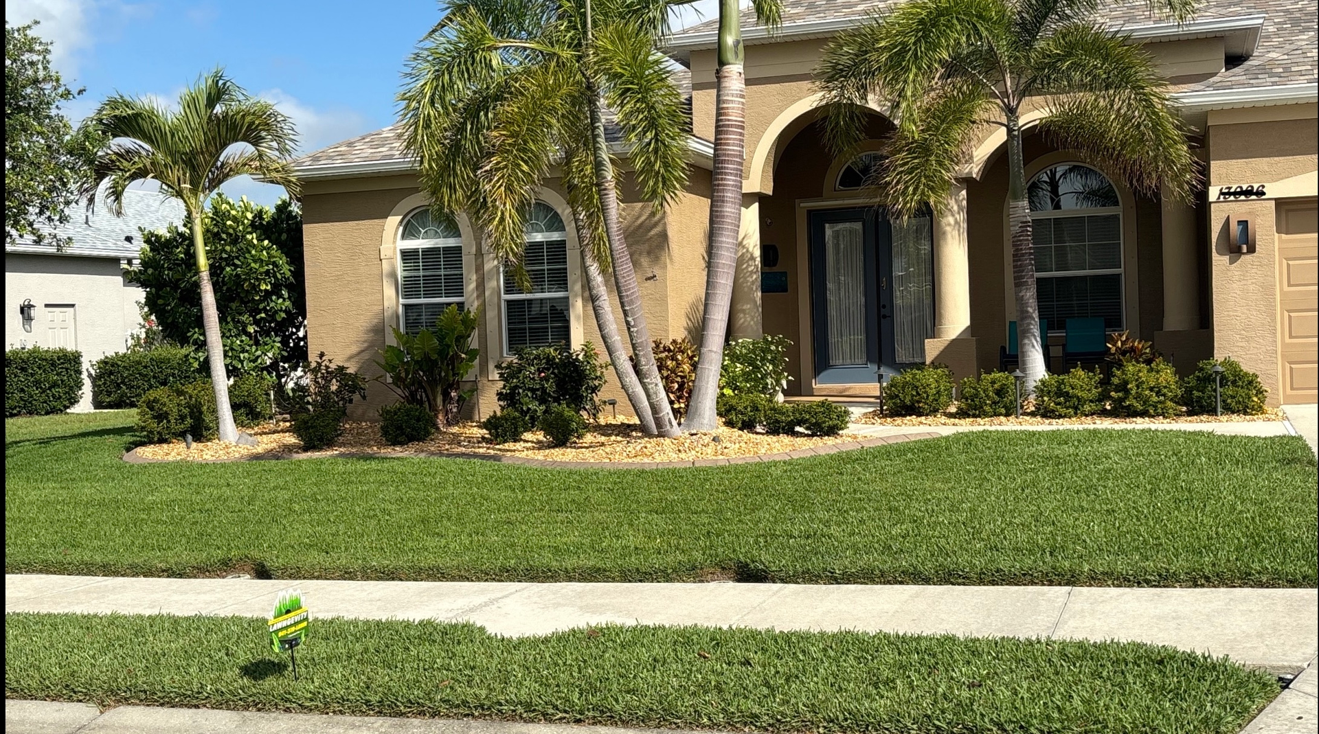 A house with a lush green lawn and palm trees in front of it.