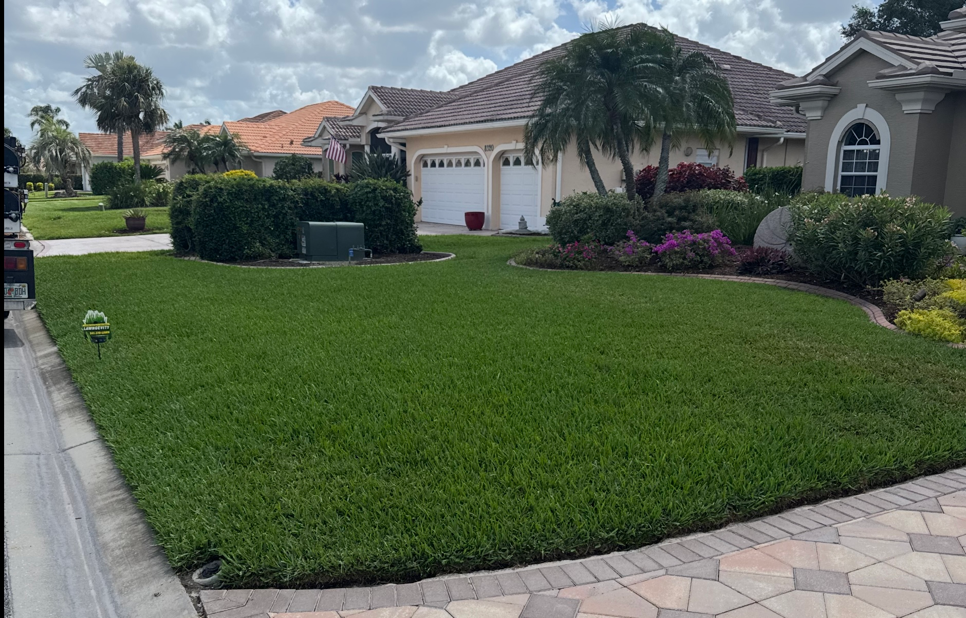 A lush green lawn in front of a house with a brick driveway.