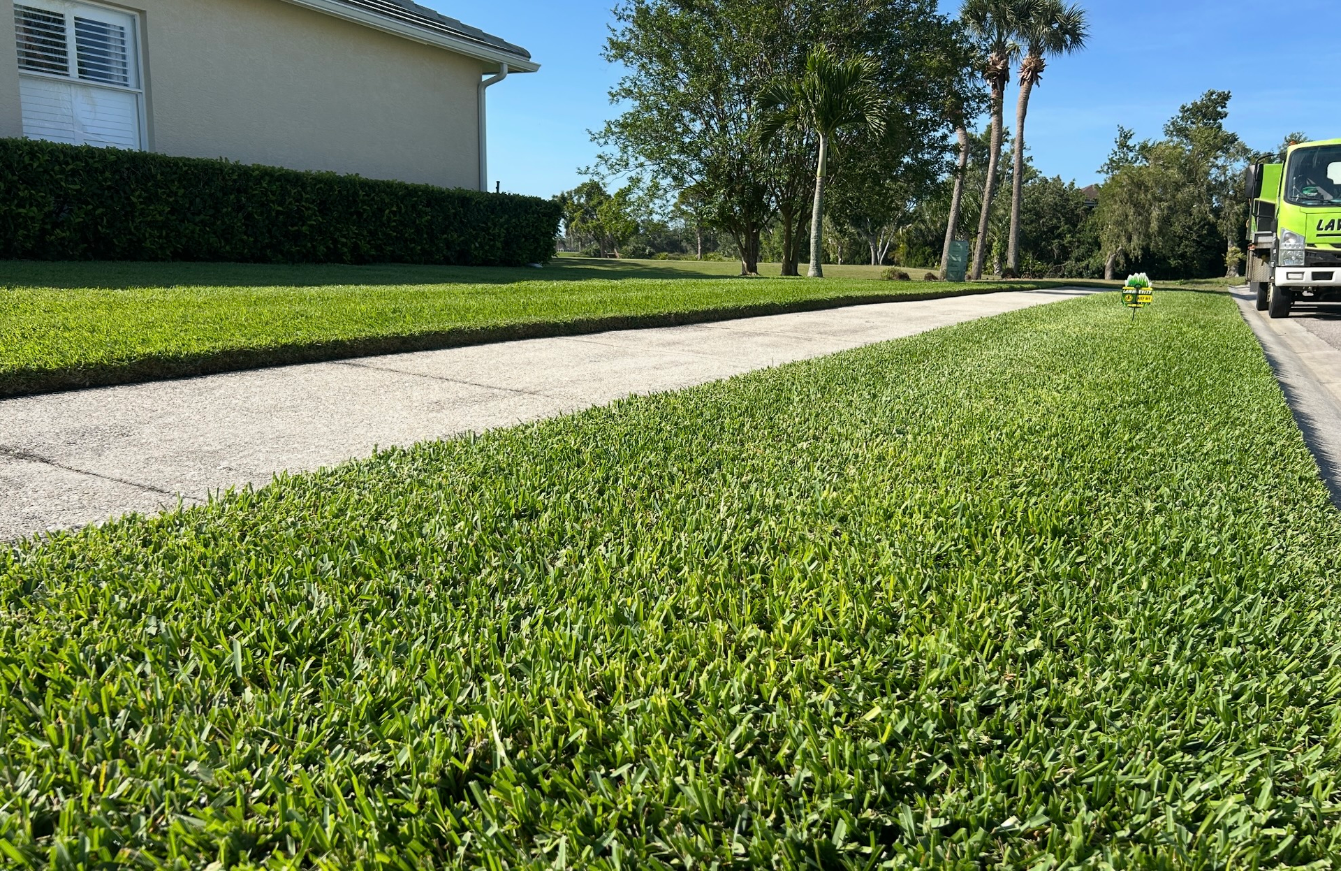 A green truck is parked on the side of the road next to a lush green lawn.