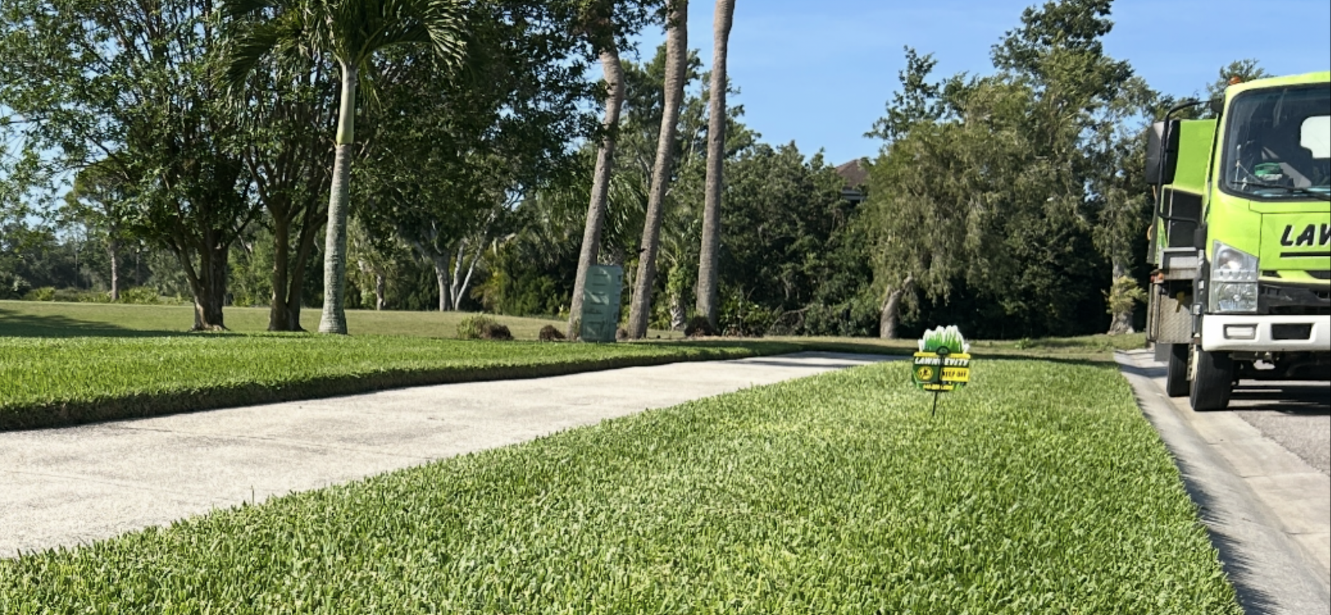 A yellow truck is driving down a road next to a lush green field.