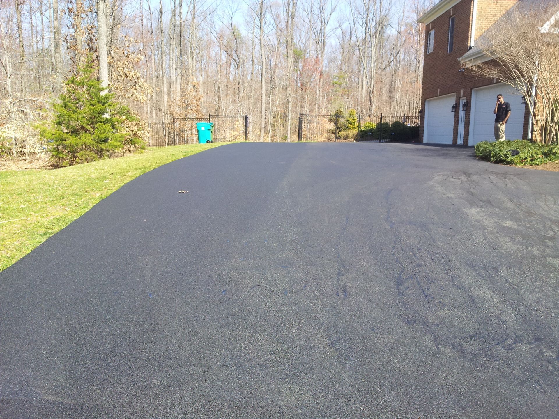 A freshly paved asphalt driveway leading to a two-car garage at a suburban home with a grassy yard and trees.