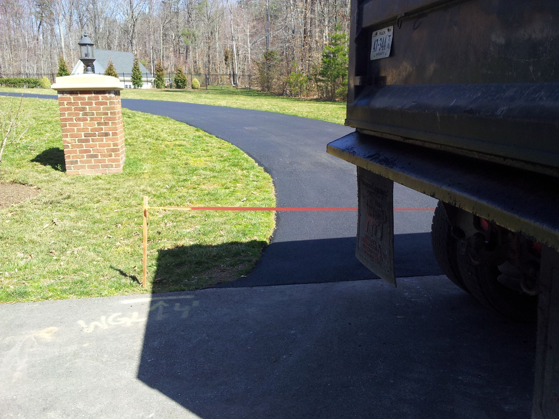 A dump truck parked on a newly paved asphalt driveway next to a brick pillar and a grassy lawn.