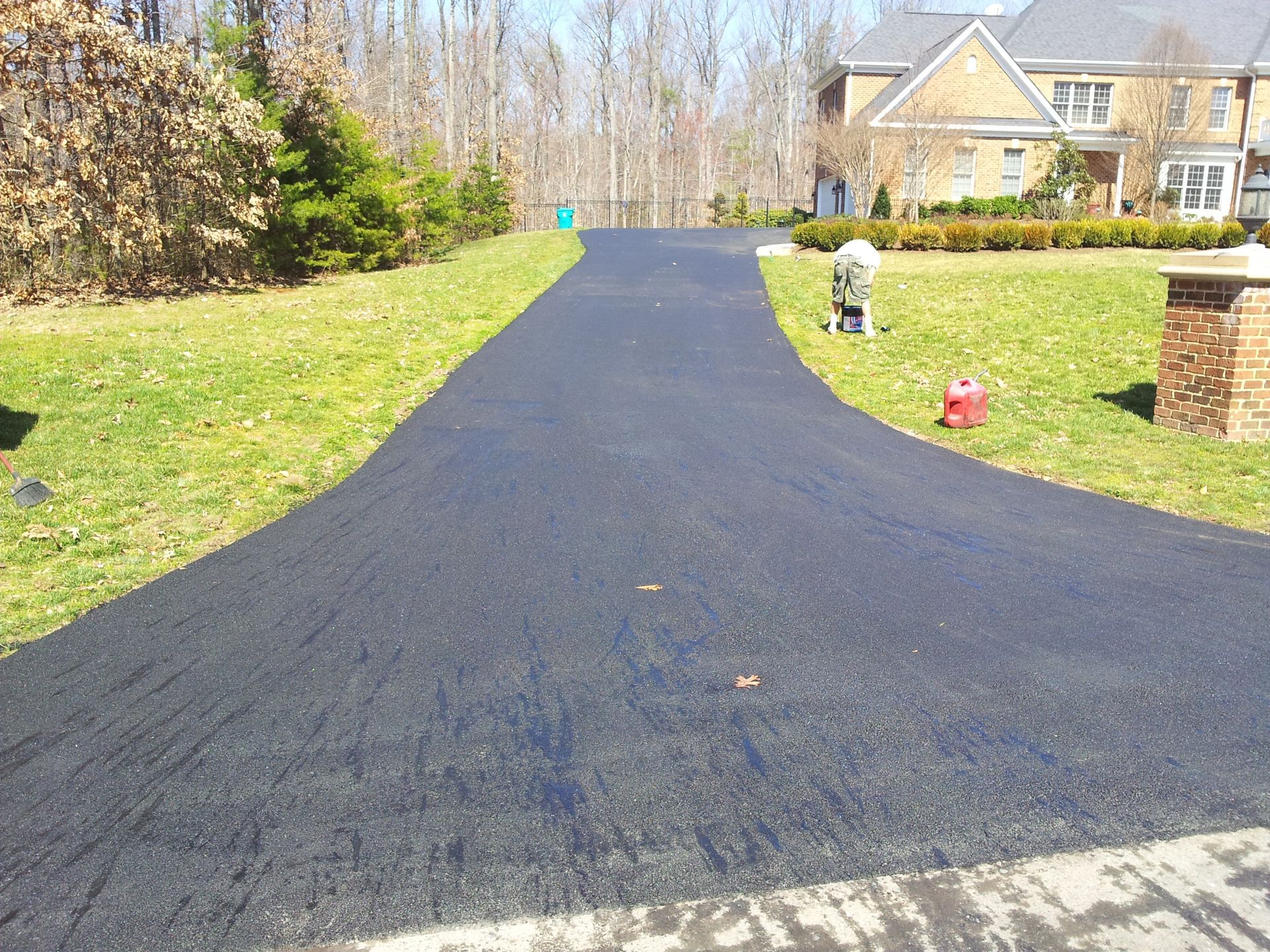 A freshly paved asphalt driveway leading toward a large brick house on a sunny day.