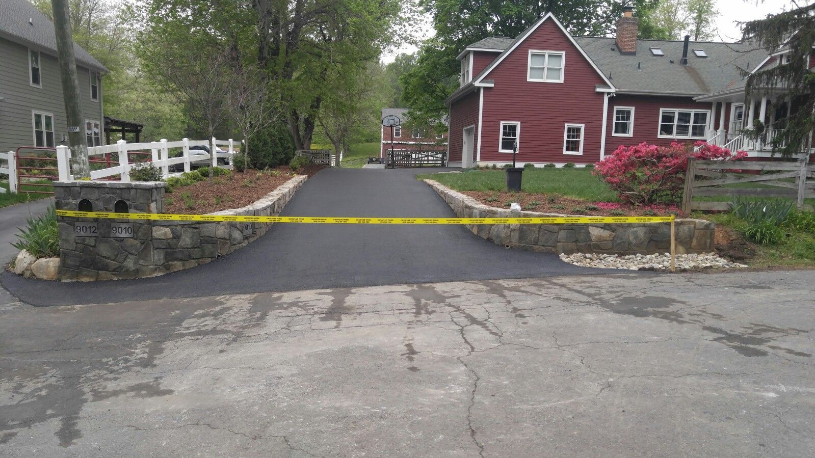 A newly paved driveway with stone walls on both sides is blocked by yellow caution tape.