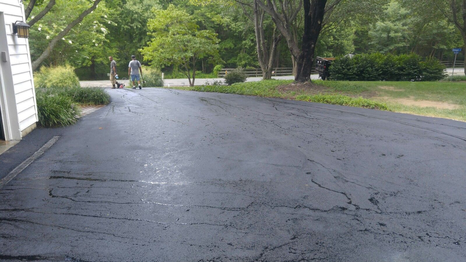 A freshly sealed asphalt driveway at a residential home with two figures standing in the distance.