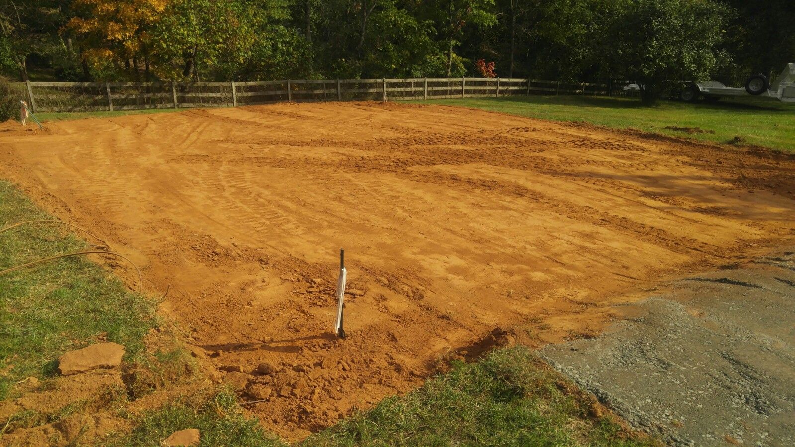 A cleared, rectangular plot of orange dirt in a grassy backyard, prepared for a new construction project.