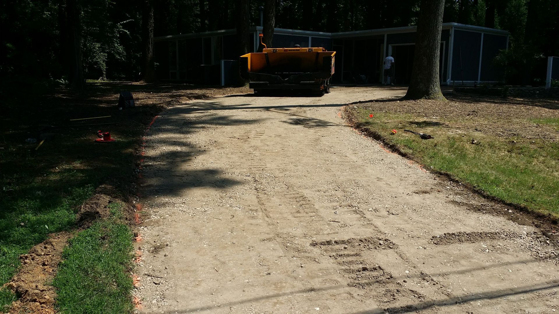 A gravel driveway leading toward a house with a yellow construction vehicle parked in front.