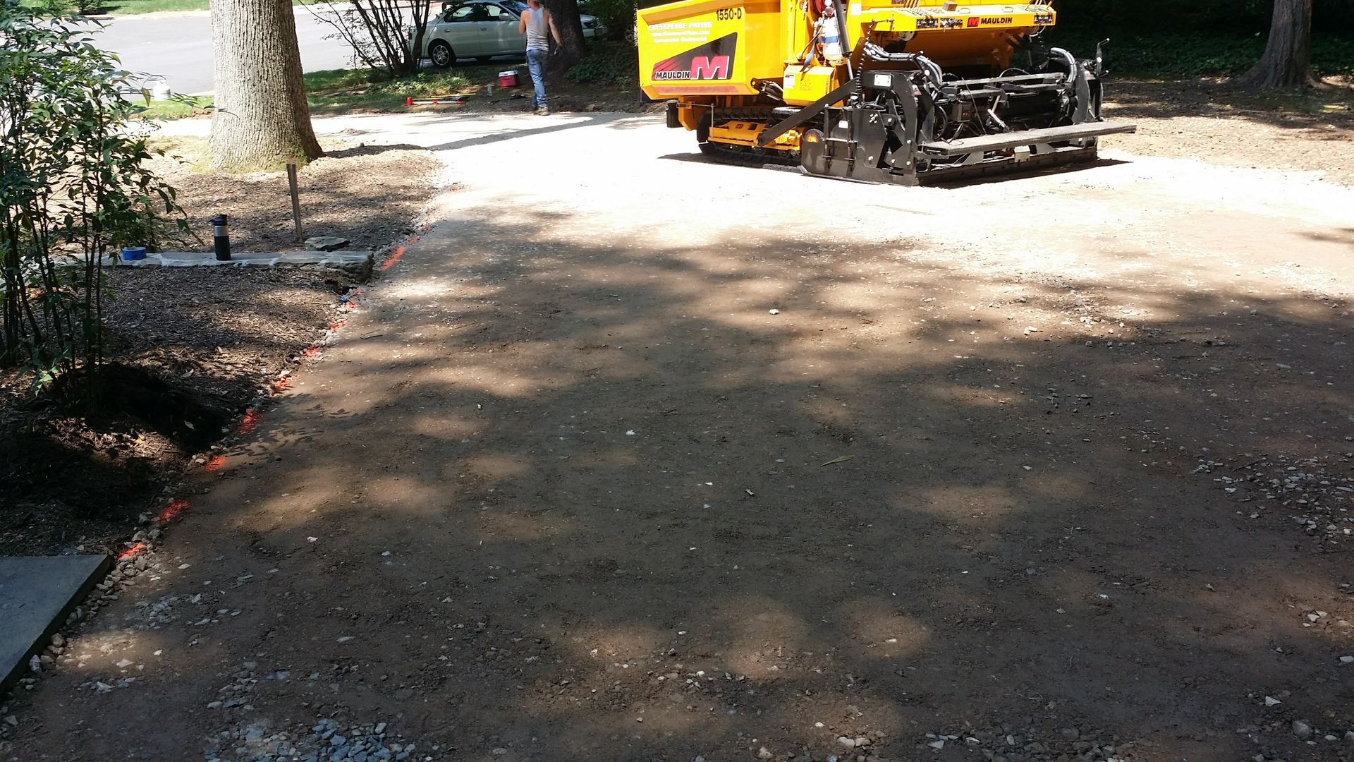 A yellow asphalt paving machine parked on a prepared gravel driveway surface in a residential area.