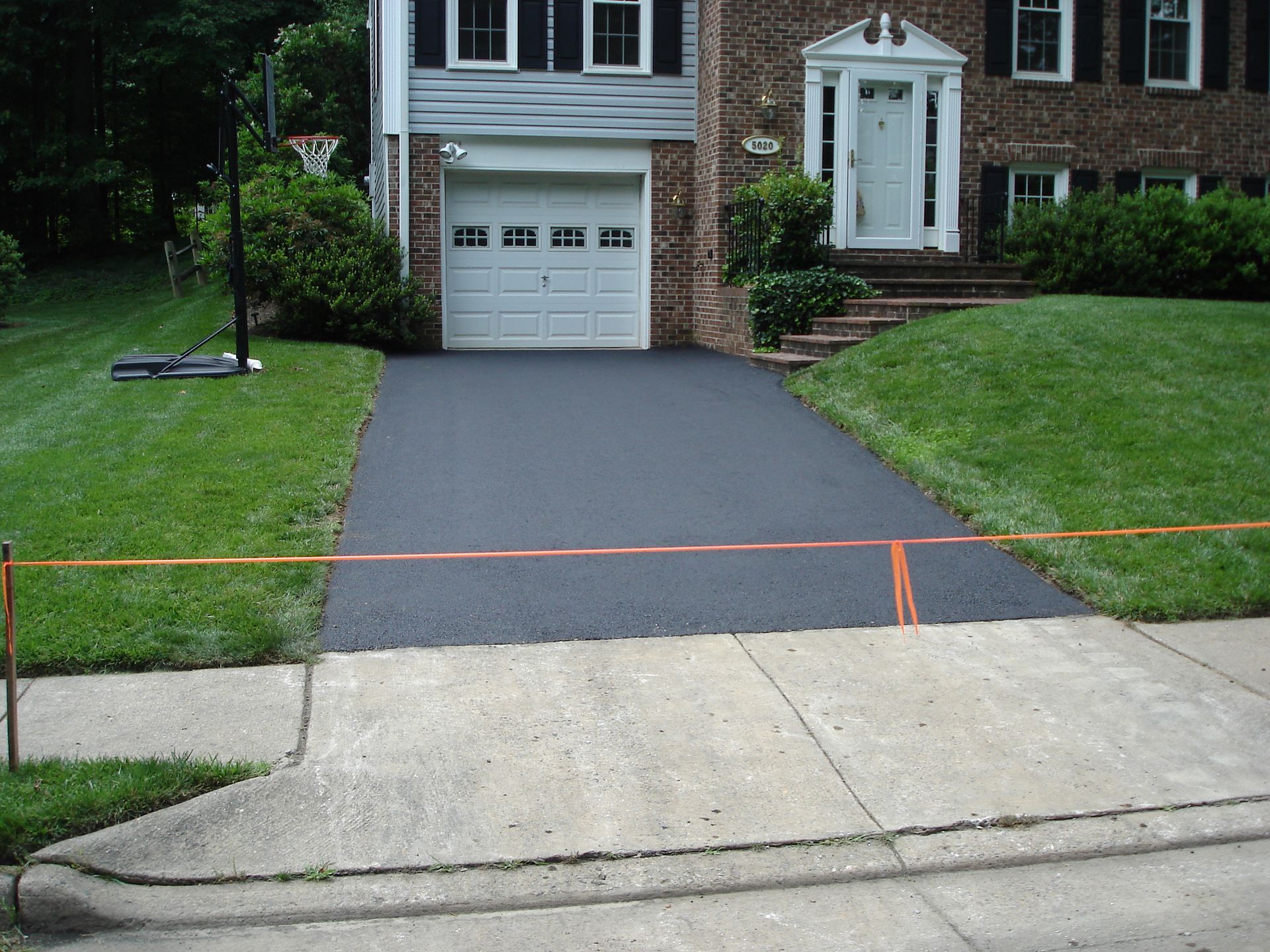 A freshly paved black asphalt driveway leading to a brick house garage, cordoned off by an orange ribbon.