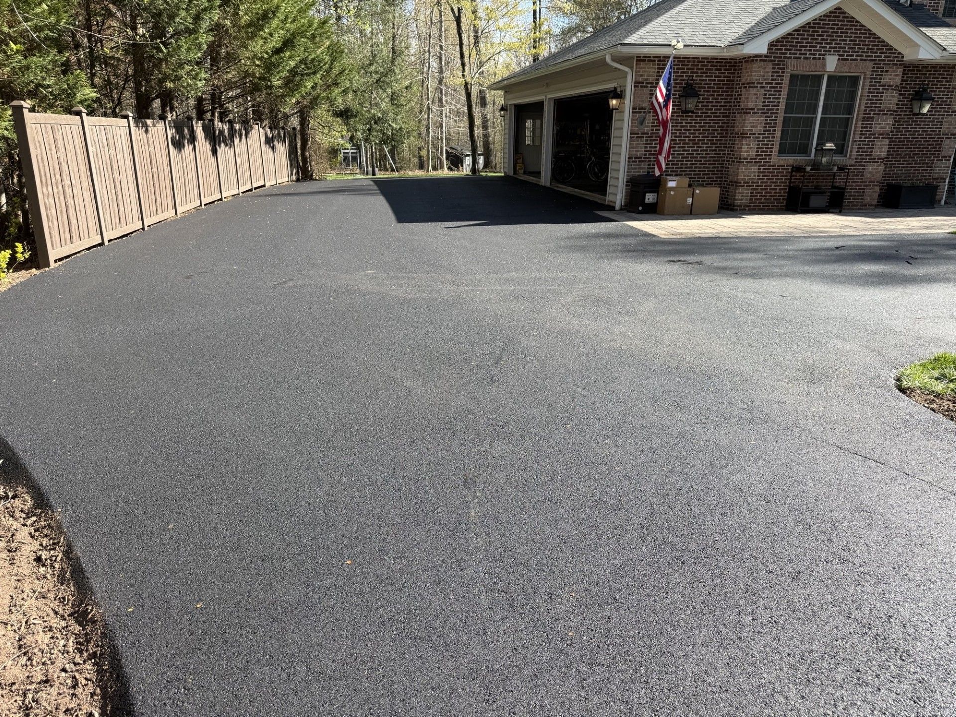 A freshly paved, dark gray asphalt driveway leads to an open multi-car garage attached to a brick residential home.