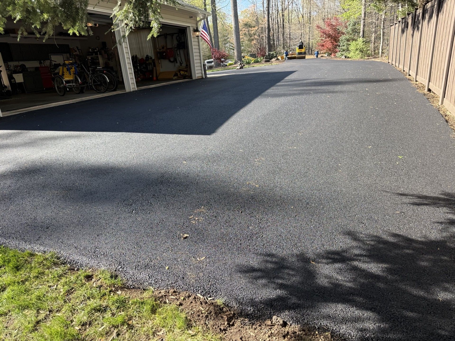 A freshly paved, dark asphalt driveway leading to an open residential garage on a sunny day.