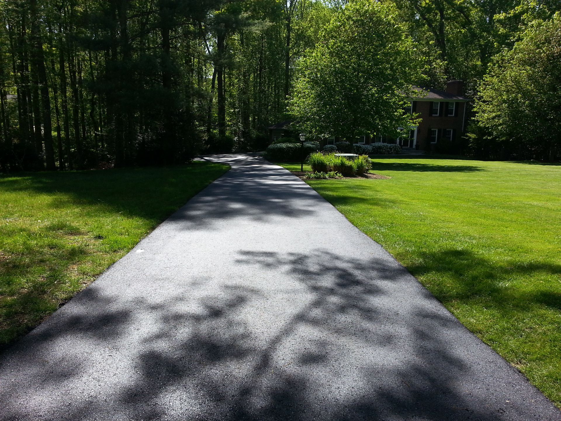 A freshly paved asphalt driveway leading toward a house framed by trees and a green lawn.