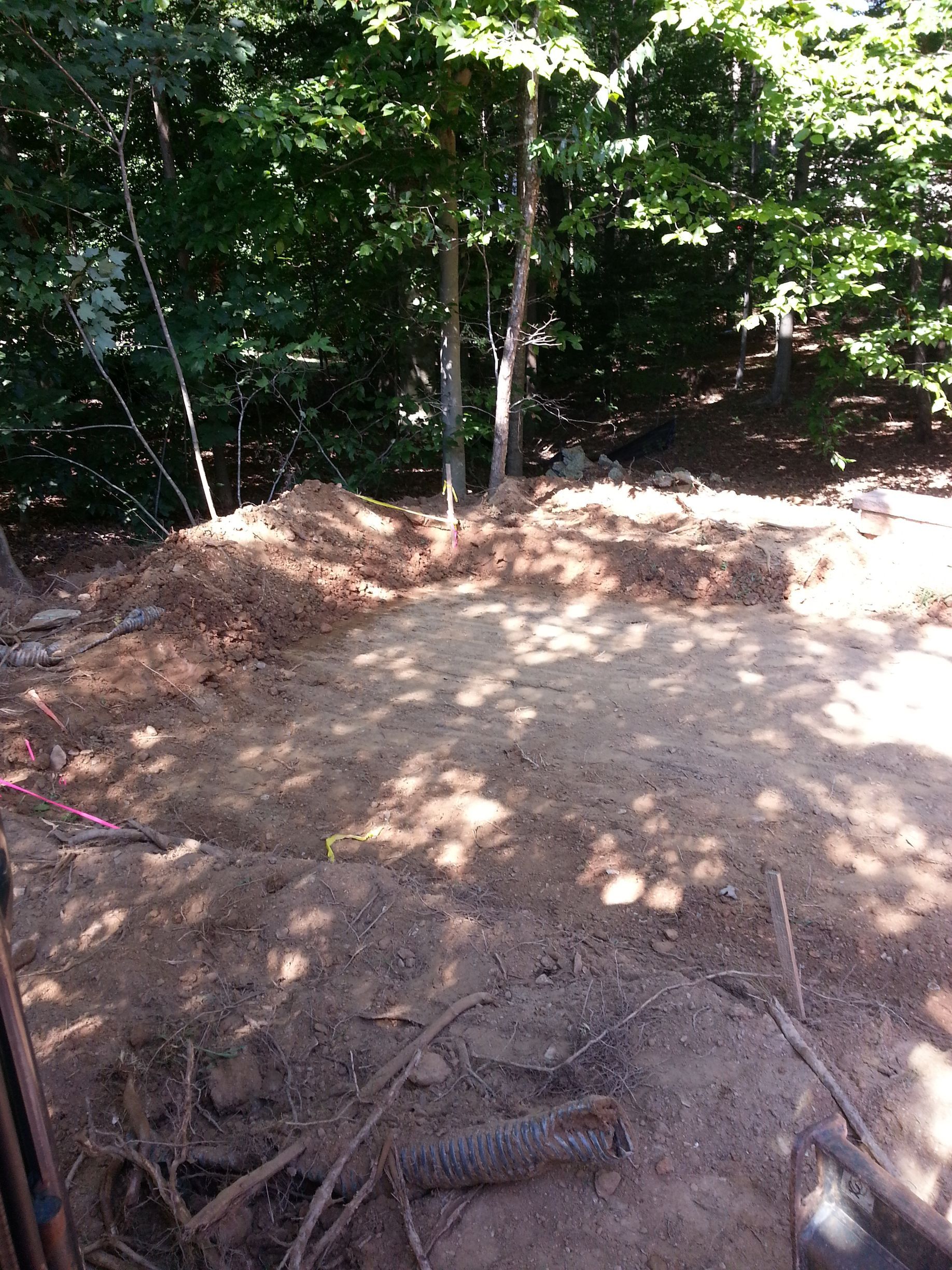 A cleared, dirt-filled area for construction in a wooded backyard with trees in the background.