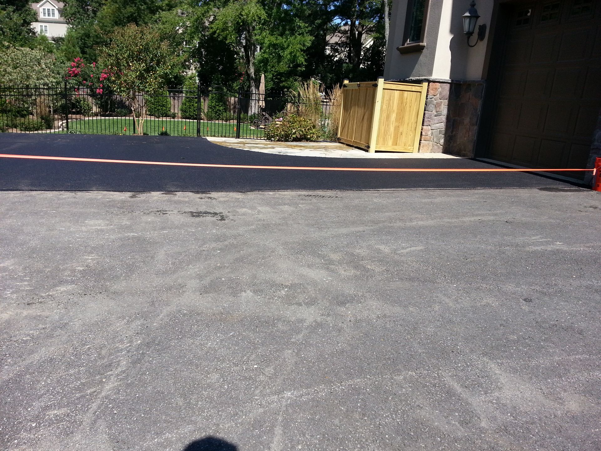 A residential driveway showing a section of freshly paved, dark asphalt alongside older, gray textured pavement.