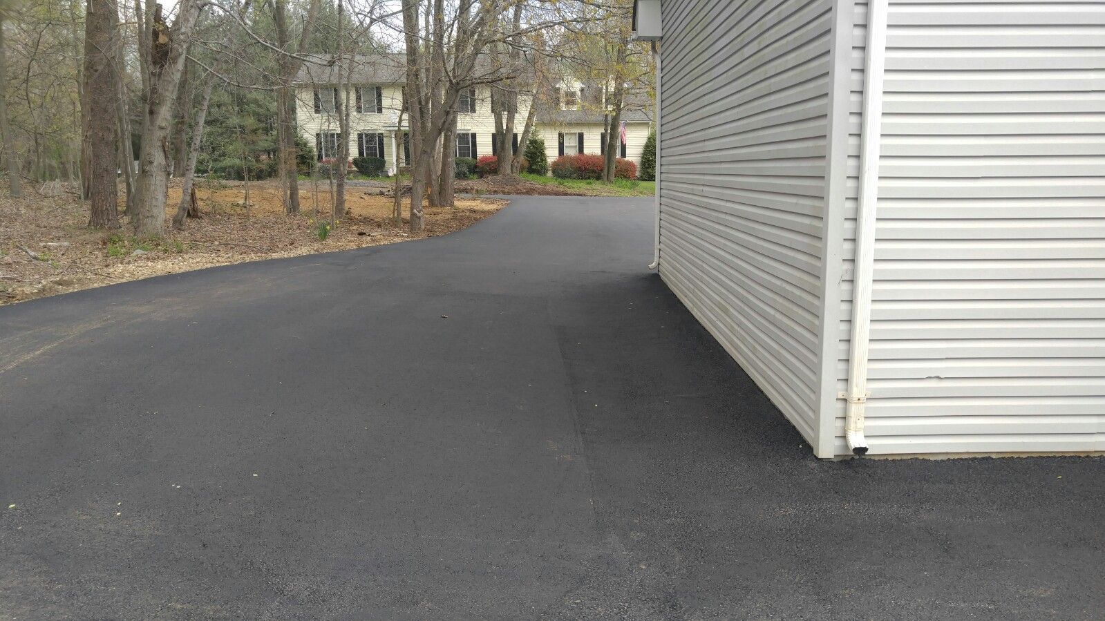 A paved driveway leading toward a house, running alongside the white, horizontal-sided wall of a garage.