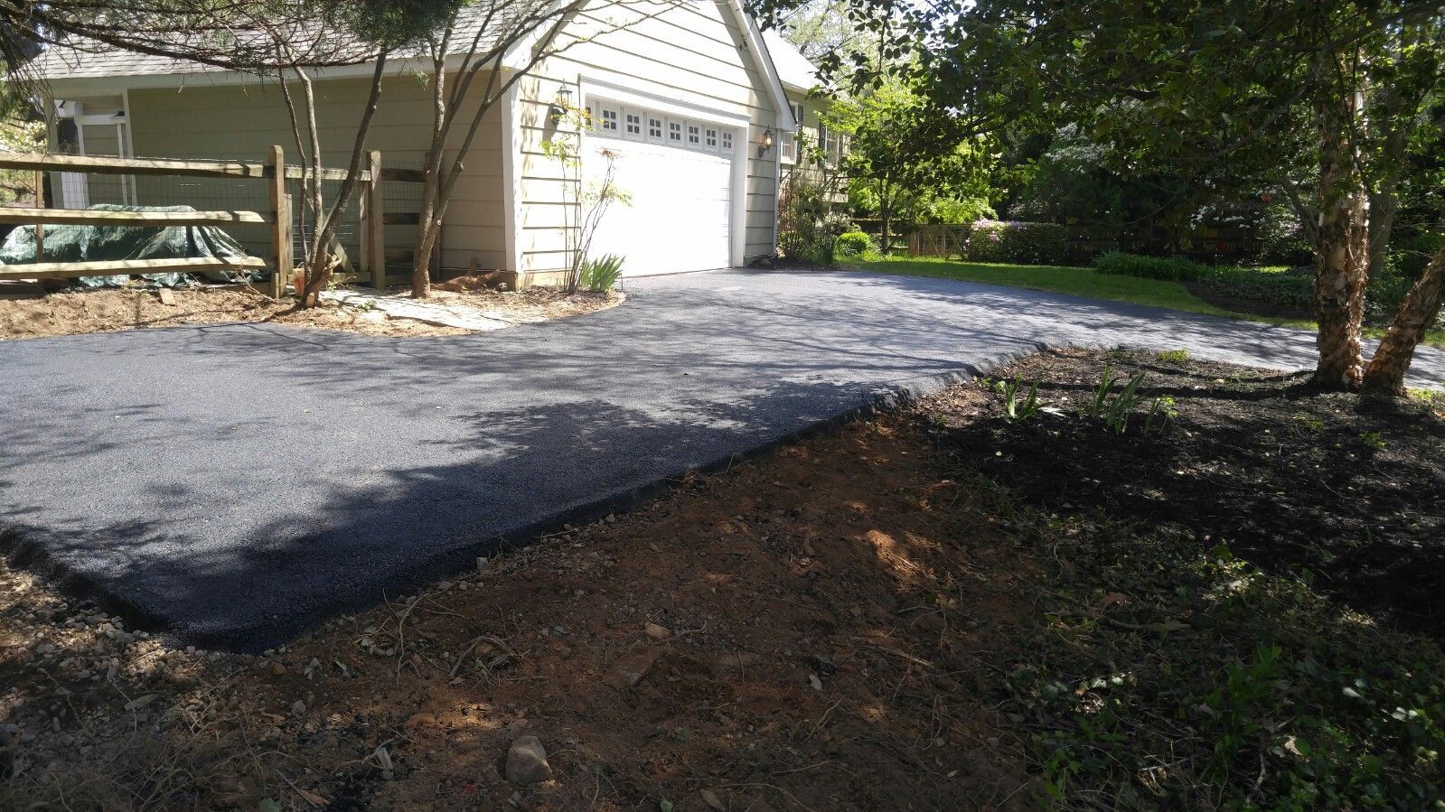 A newly laid, dark gray crushed stone driveway leads to a garage, with a patch of bare soil in the foreground.