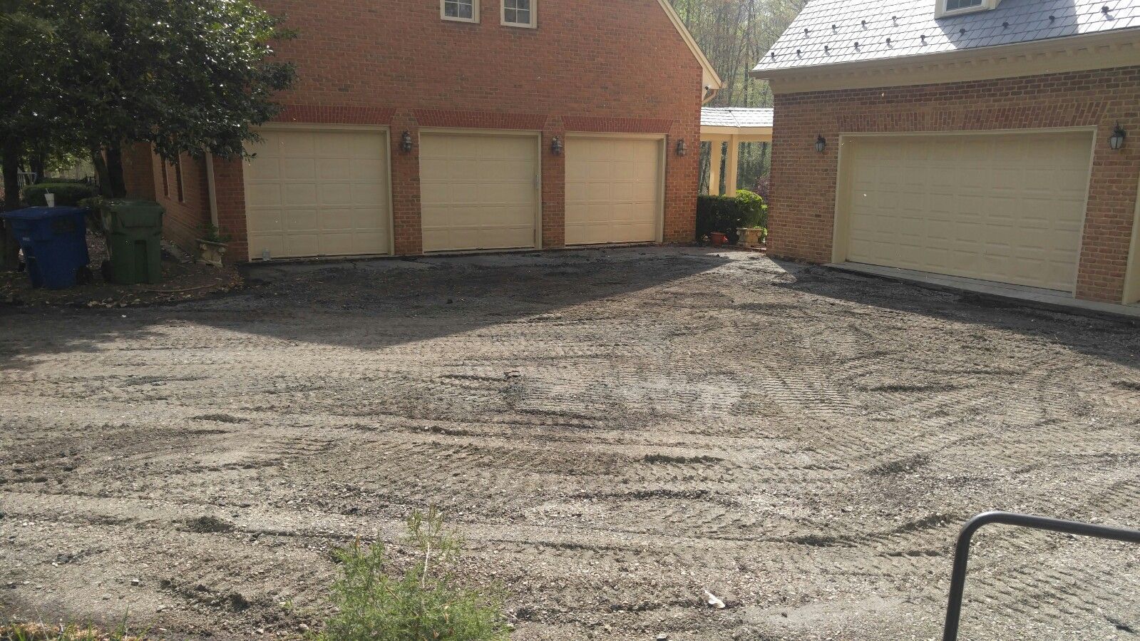 A brick house with four garage bays facing a large, unpaved gravel driveway.