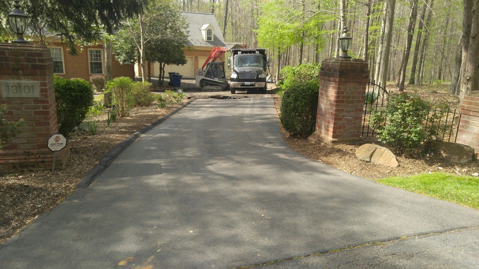 A residential driveway leads toward a house with a construction truck and equipment parked in front.
