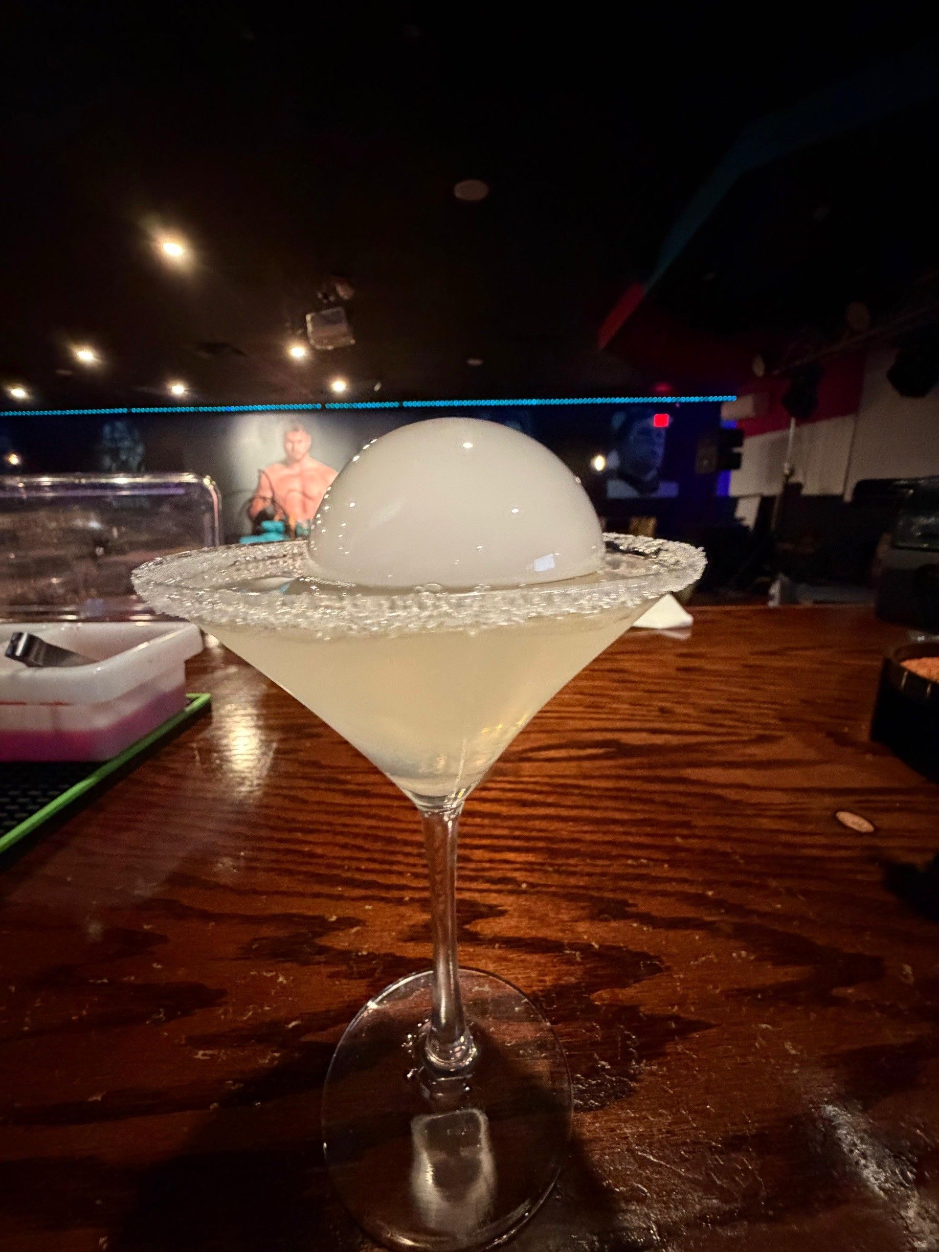 Martini glass with sugar rim and bubble, on a bar. Dark bar setting.