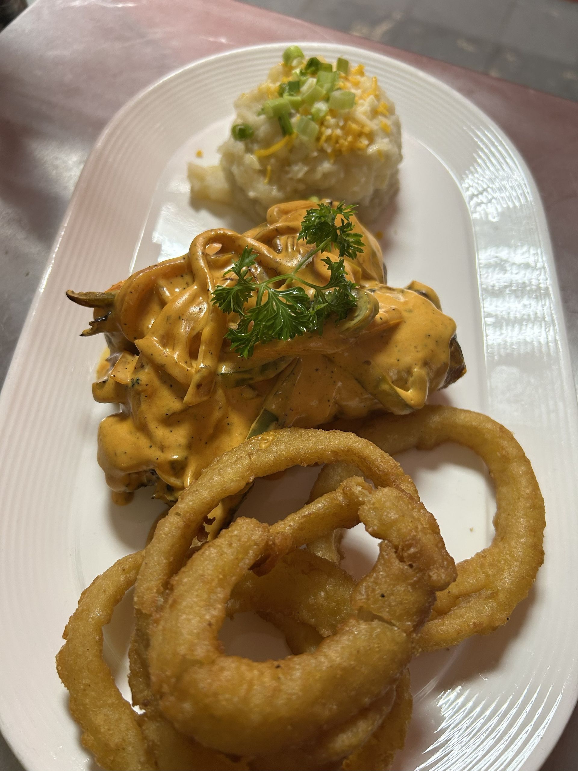 Chicken dish with sauce, potato salad, and onion rings on a white platter.