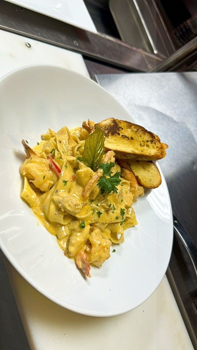 Pasta dish with shrimp in creamy sauce, garnished with parsley and garlic bread.