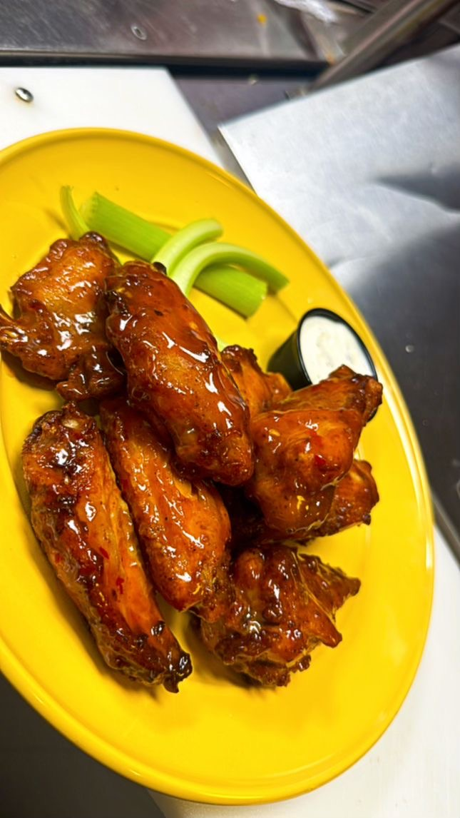 Chicken wings on yellow plate with celery and dipping sauce.