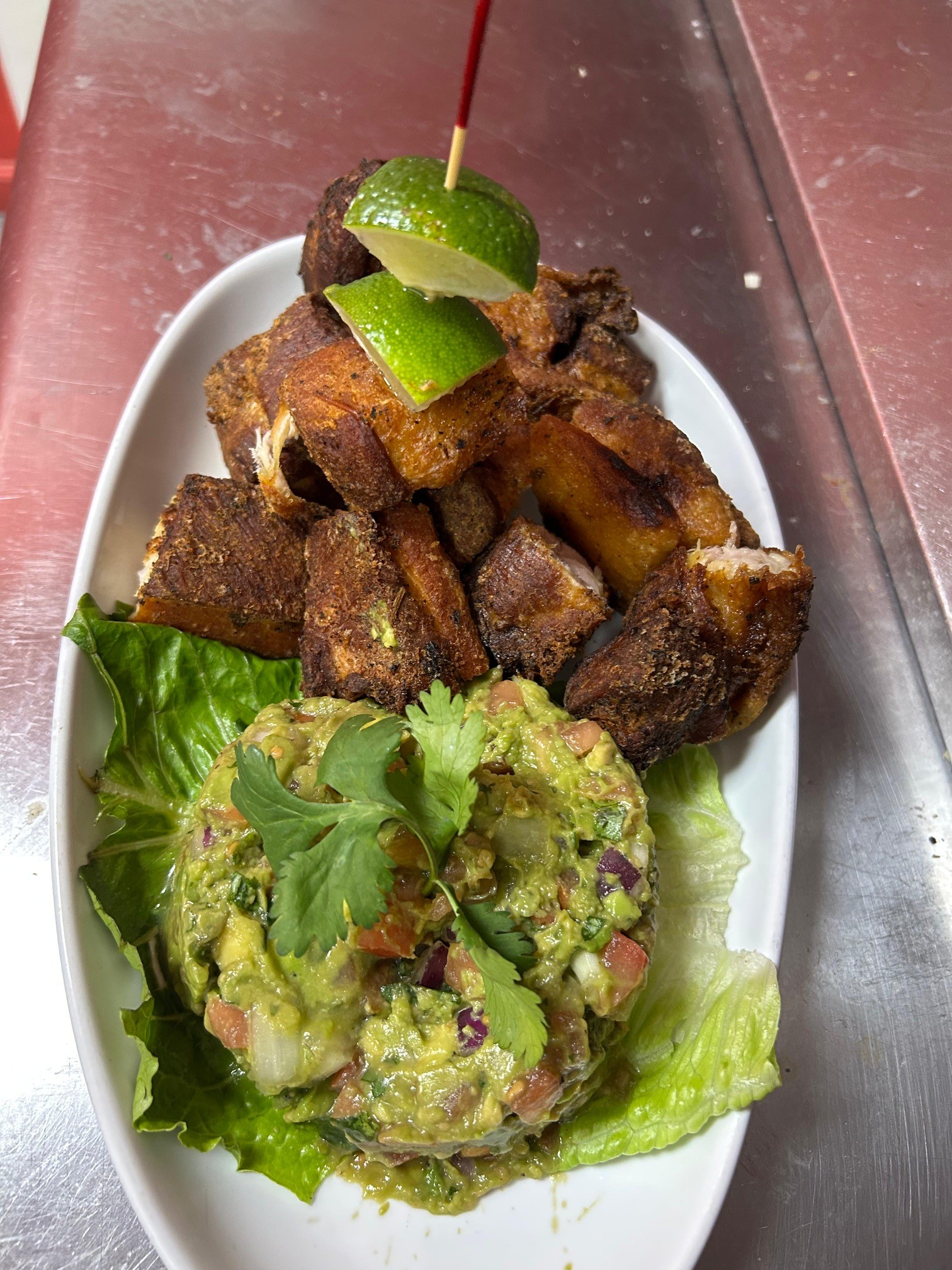 Fried plantains and guacamole on a white plate, garnished with lime and cilantro.