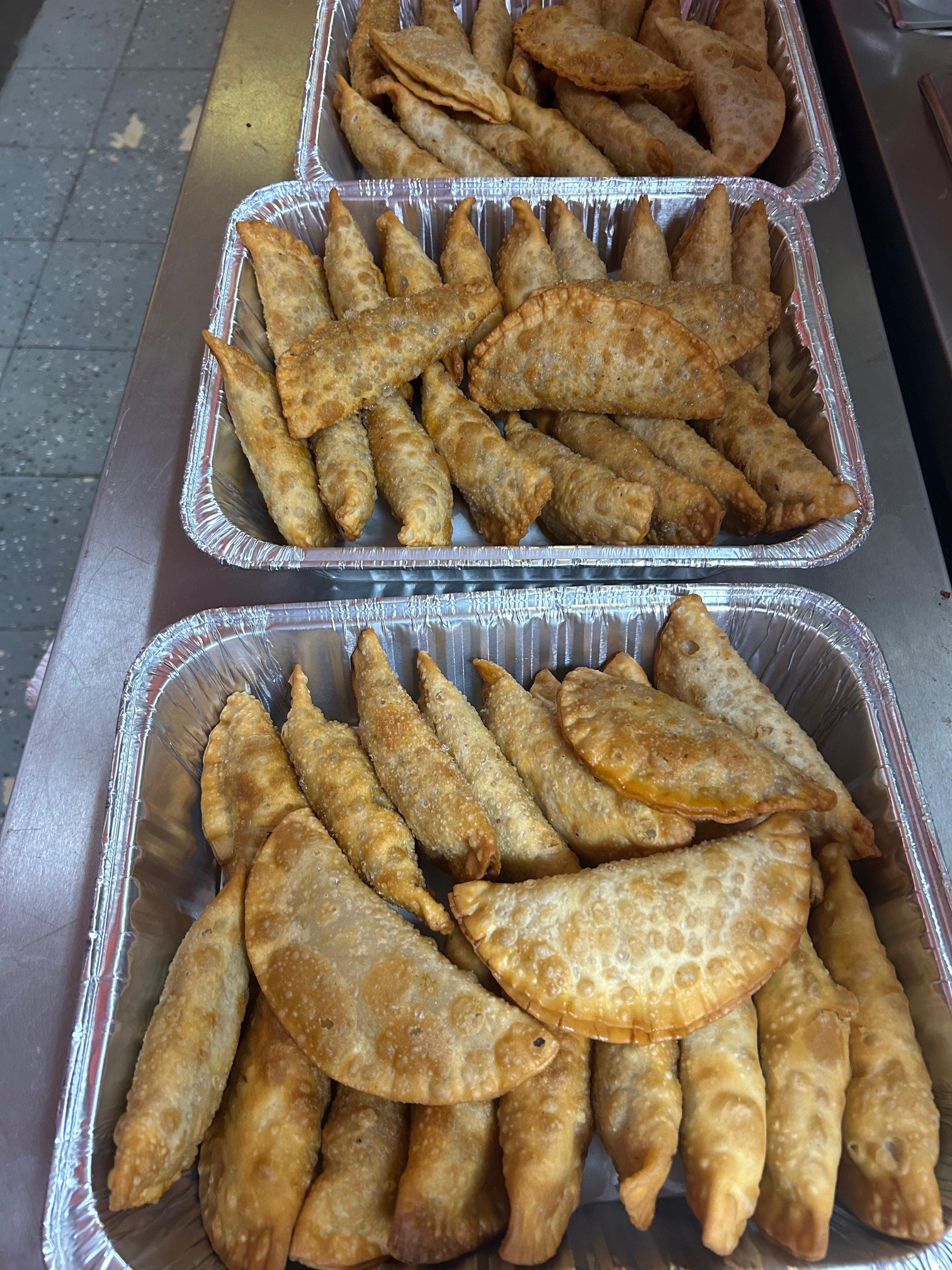 Three trays of golden-brown empanadas, likely a catered or prepared food service.