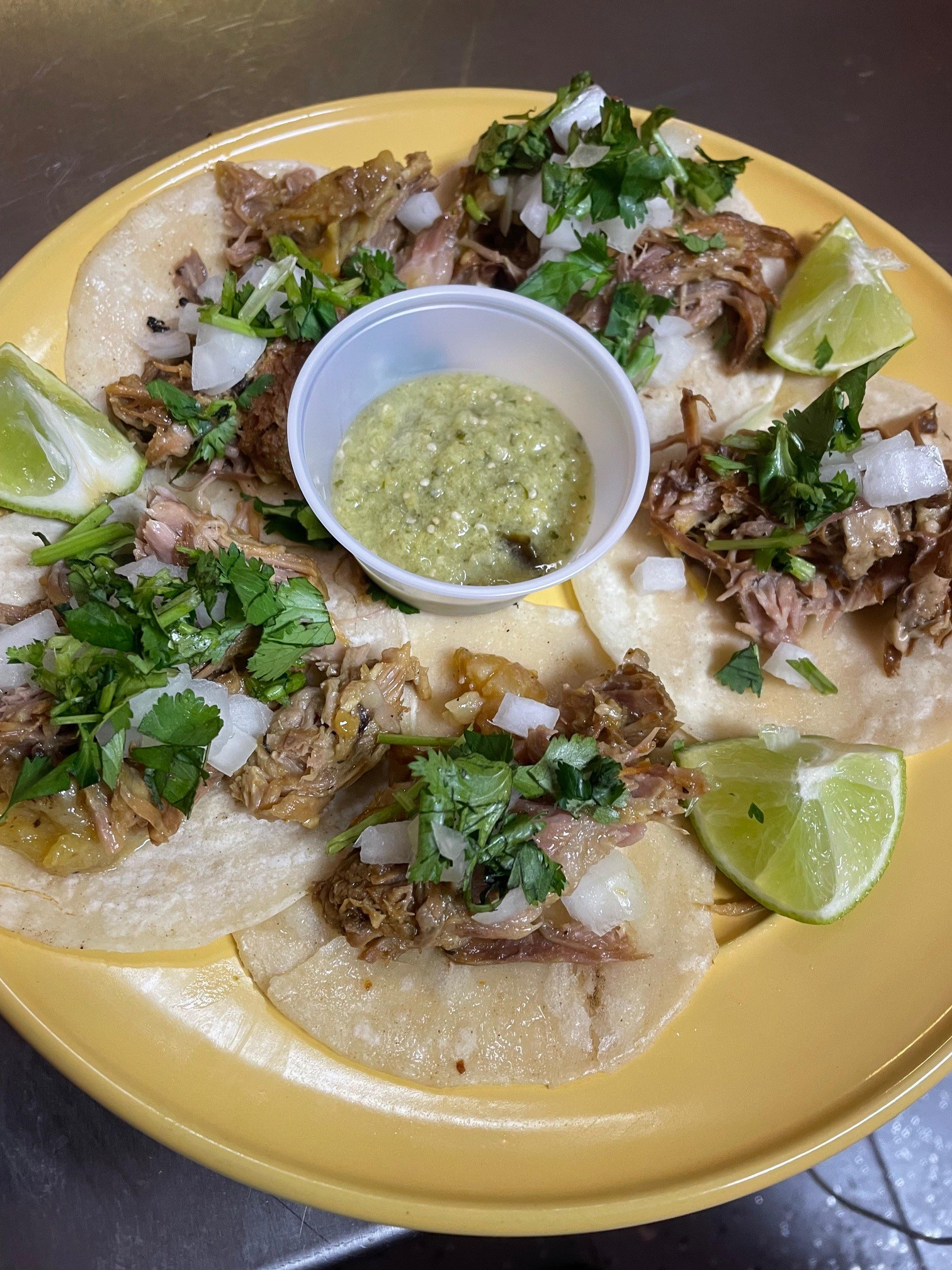 Plate of tacos with meat, onions, cilantro, salsa, and lime wedges.