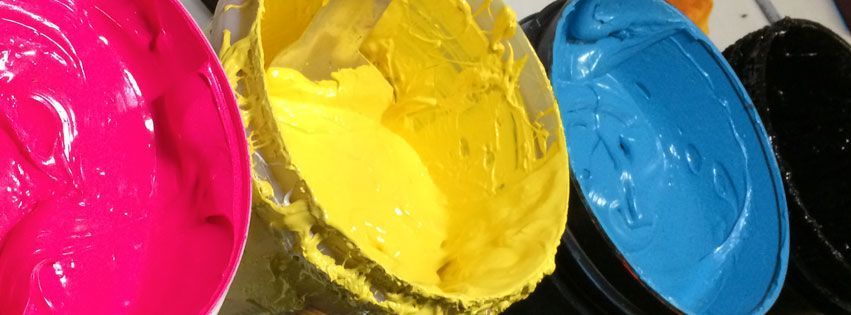 Close-up of four round containers holding thick, vibrant magenta, yellow, cyan, and black printing ink.