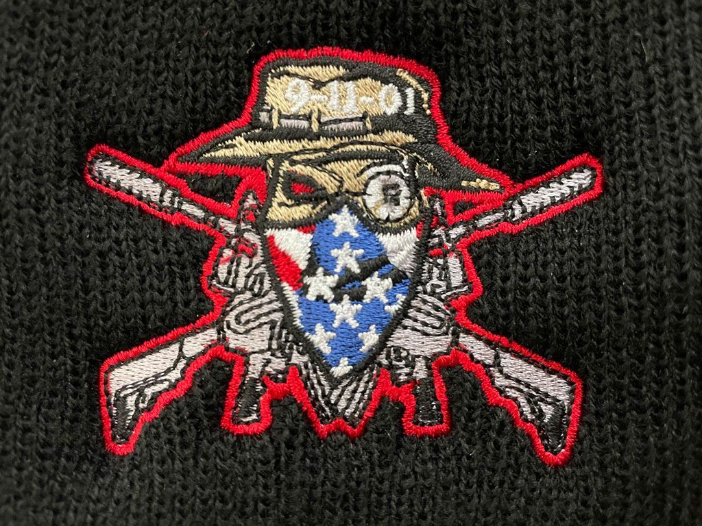 An embroidered patch on black fabric featuring a skull wearing a hat marked 