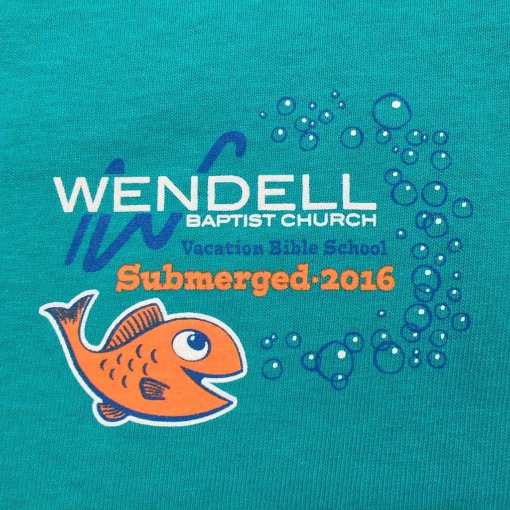 A teal t-shirt with a cartoon orange fish and bubbles, promoting Wendell Baptist Church Vacation Bible School 2016.