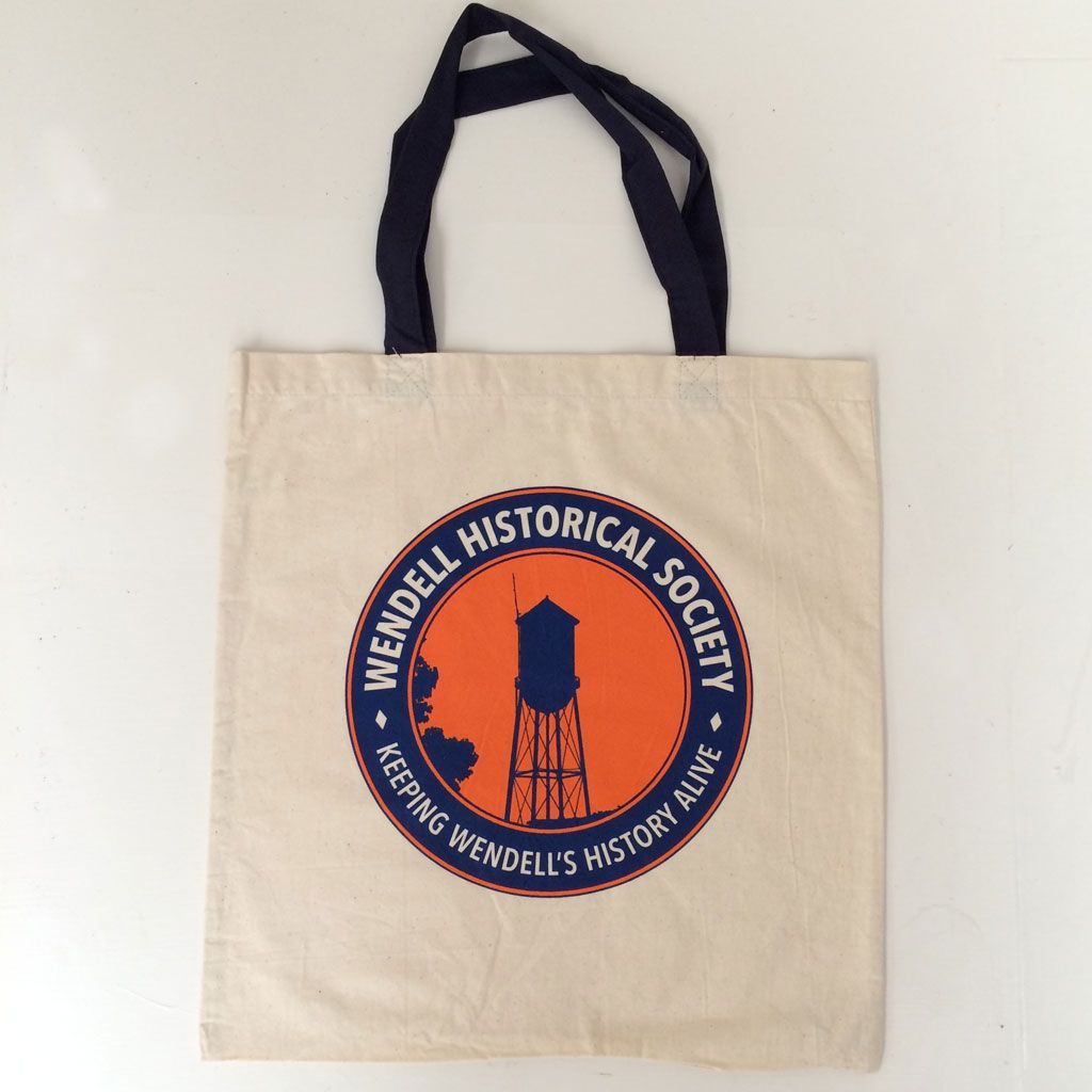 A natural-colored canvas tote bag with a dark blue circular logo featuring a water tower and 