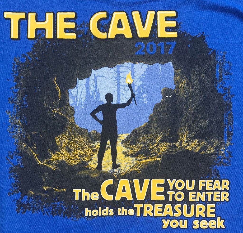 A person with a torch stands in a cave entrance looking out at a forest, with the quote about the treasure you seek.