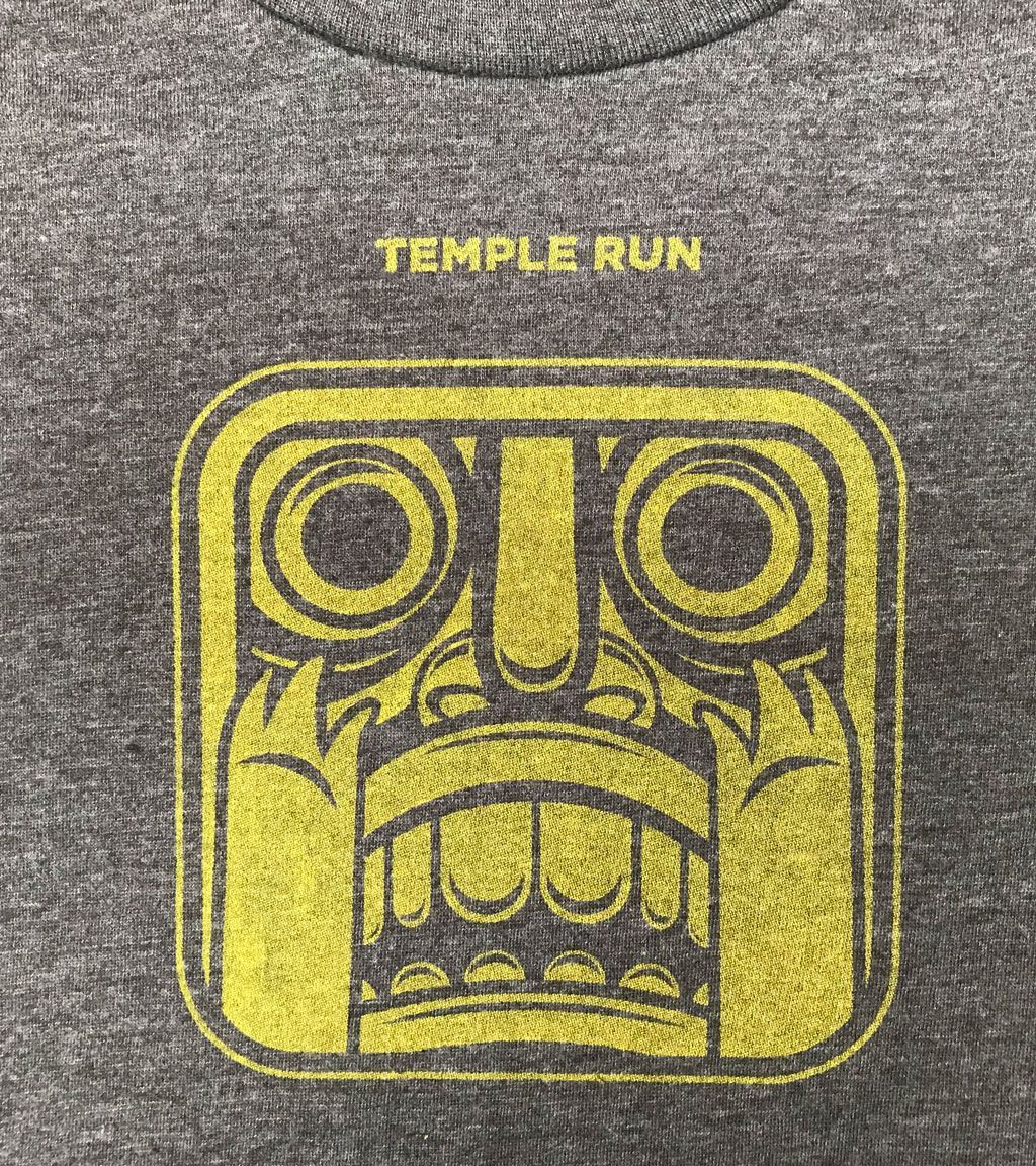 A close-up of a grey t-shirt featuring the yellow Temple Run idol icon.