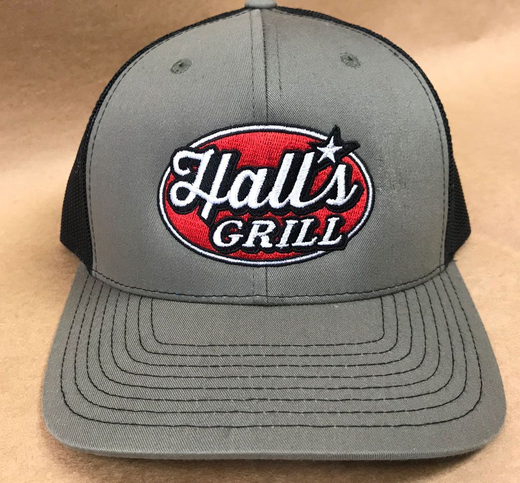 A grey and black trucker hat featuring an embroidered red oval patch that reads 