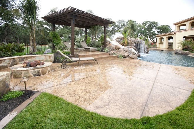 Stone patio with pergola, built-in seating, and a waterfall flowing into a backyard pool